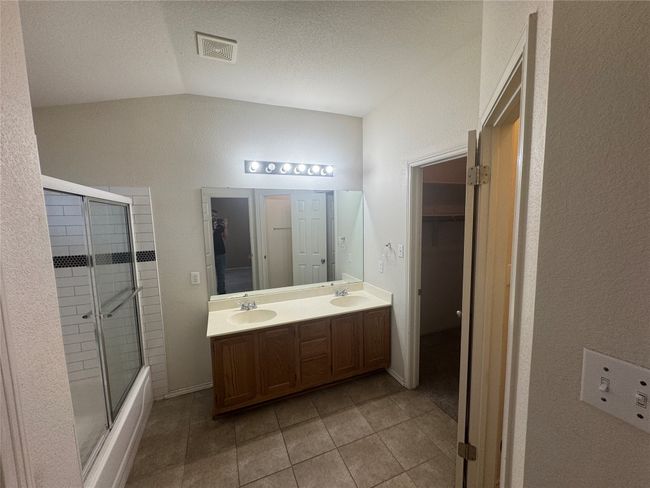Full bath featuring double vanity, tile patterned floors, vaulted ceiling, combined bath / shower with glass door, and a spacious closet | Image 7