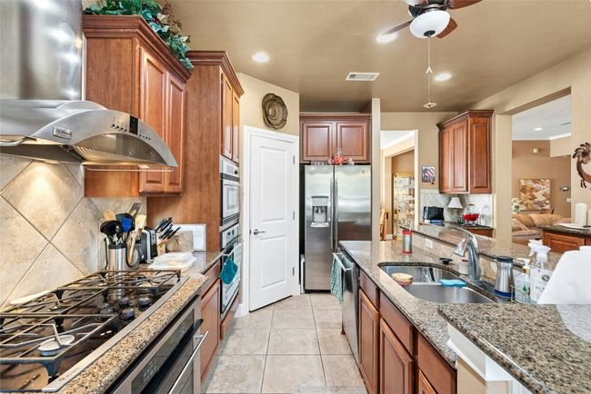 Kitchen featuring extractor fan, stainless steel appliances, tasteful backsplash, ceiling fan, and light stone counters | Image 7