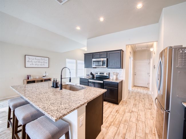Kitchen featuring stainless steel appliances, sink, light stone counters, a breakfast bar, and a center island with sink | Image 5