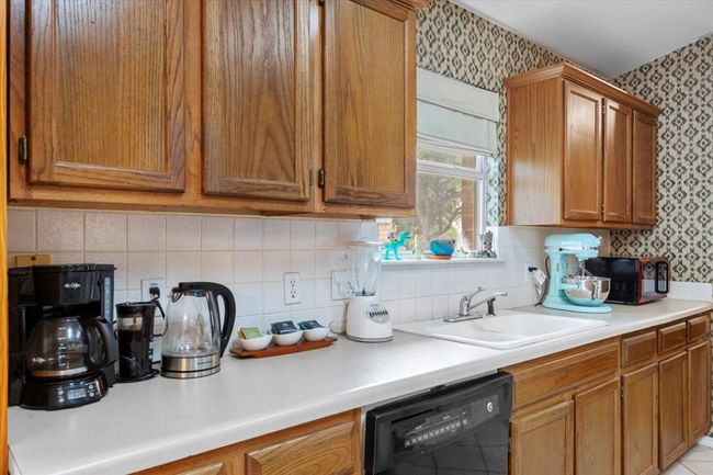 Kitchen with black appliances, wallpapered walls, a sink, light countertops, and brown cabinets | Image 11