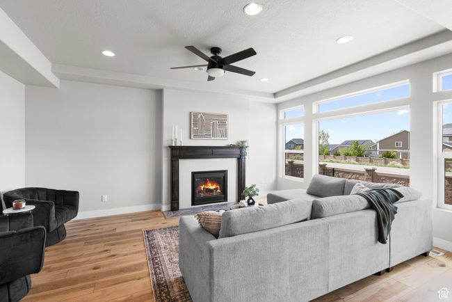 Living room with light wood-type flooring, a wealth of natural light, ceiling fan, and a glass covered fireplace | Image 6