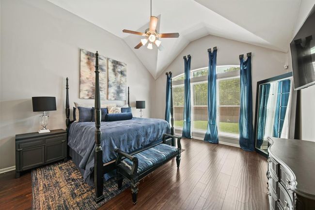 Bask in the serene beauty of the spacious primary retreat, featuring a dramatic vaulted ceiling, rich wood flooring, and a wall of windows that fill the space with natural light. | Image 25
