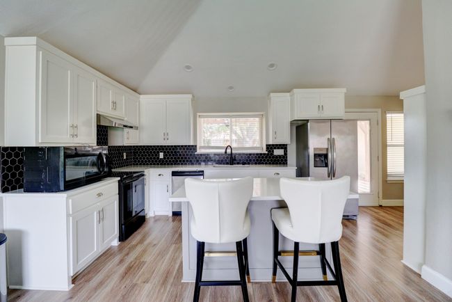 Kitchen with black appliances, under cabinet range hood, a breakfast bar, white cabinets, and vaulted ceiling | Image 9