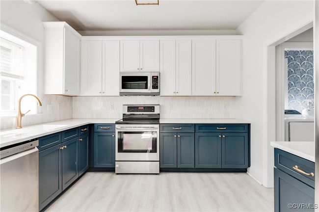Kitchen featuring appliances with stainless steel finishes, washer / dryer, white cabinets, and light wood-type flooring | Image 16