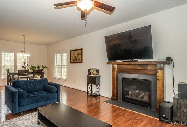 Living room featuring ceiling fan with notable chandelier, a fireplace with flush hearth, baseboards, and wood finished floors | Image 7