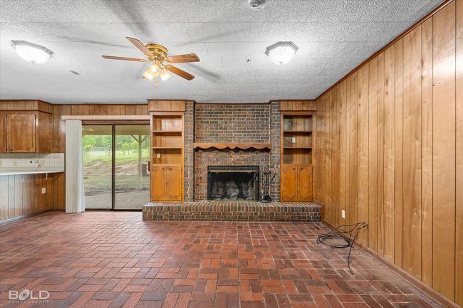 Unfurnished living room with wooden walls, brick flooring, a ceiling fan, and baseboards | Image 10