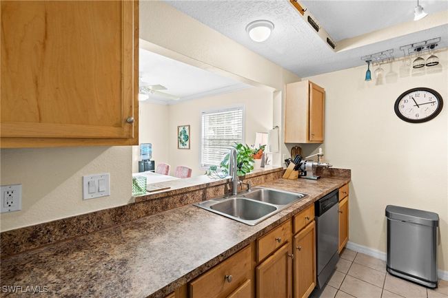 Kitchen featuring light tile patterned floors, baseboards, a textured ceiling, stainless steel dishwasher, and a sink | Image 12