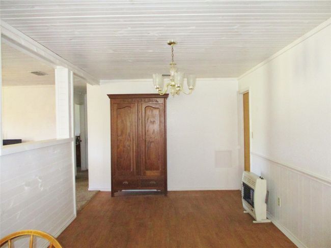 Unfurnished dining area featuring heating unit, visible vents, wainscoting, wood finished floors, and a chandelier | Image 11