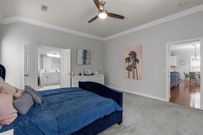 Bedroom with ensuite bathroom, light carpet, baseboards, ornamental molding, and visible vents | Image 24