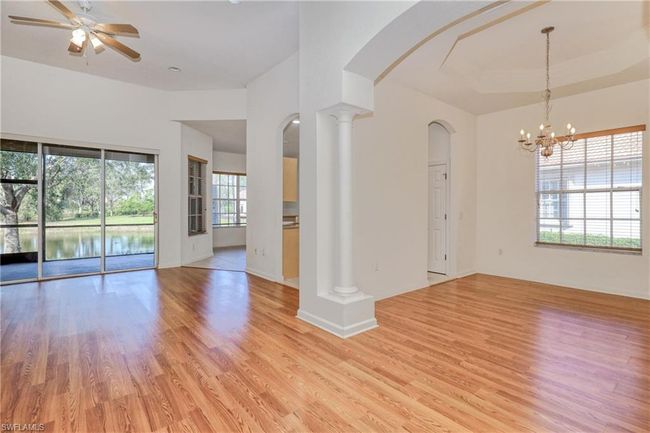 Unfurnished living room with a tray ceiling, ceiling fan with notable chandelier, light hardwood / wood-style flooring, and ornate columns | Image 16