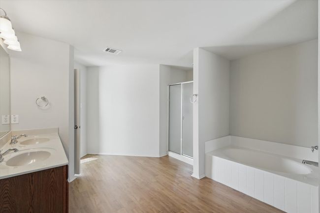 Bathroom featuring a shower stall, wood finished floors, a bath, and double vanity | Image 13