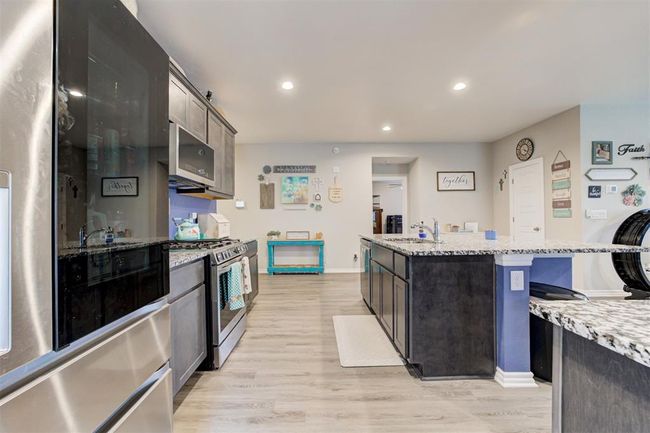 Kitchen featuring stainless steel gas range, refrigerator, light wood finished floors, an island with sink, and light stone countertops | Image 15