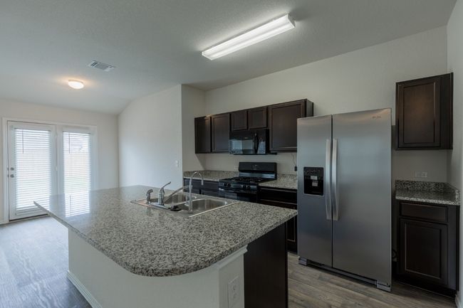 Kitchen featuring black appliances, a sink, wood finished floors, dark brown cabinetry, and a kitchen island with sink | Image 6