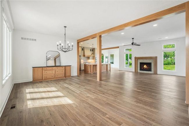 Unfurnished living room with light wood finished floors, ceiling fan, a chandelier, a warm lit fireplace, and baseboards | Image 16