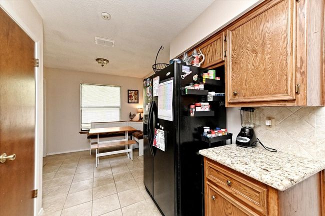 Kitchen with tasteful backsplash, black fridge, brown cabinetry, and light tile patterned floors | Image 11