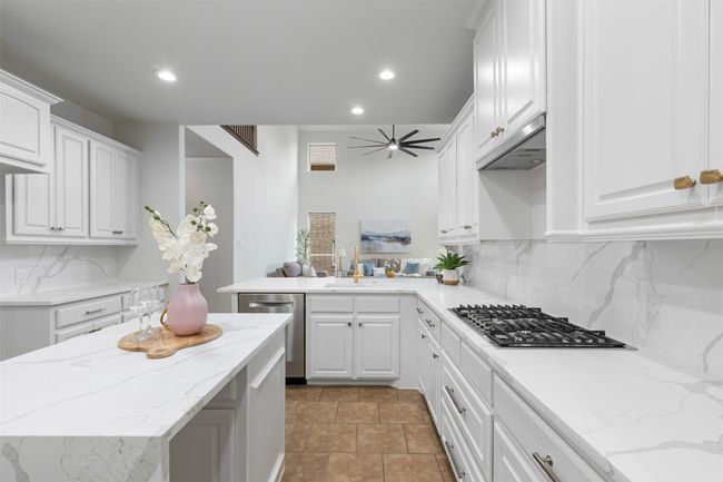Kitchen with under cabinet range hood, appliances with stainless steel finishes, white cabinets, backsplash, and a sink | Image 7