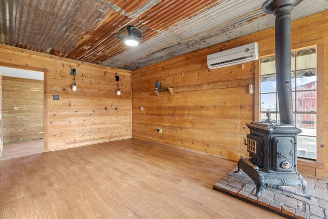 Empty room with a wood stove, a wall unit AC, wooden walls, and wood finished floors | Image 13