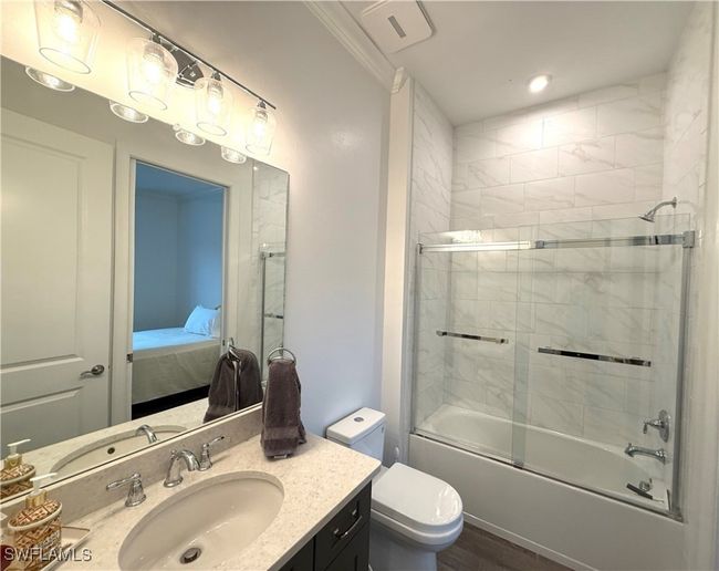 Ensuite bathroom with vanity, enclosed tub / shower combo, wood finished floors, and ornamental molding | Image 21