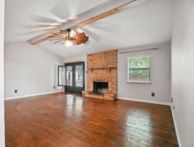Unfurnished living room featuring a ceiling fan, a brick fireplace, wood finished floors, and french doors | Image 6