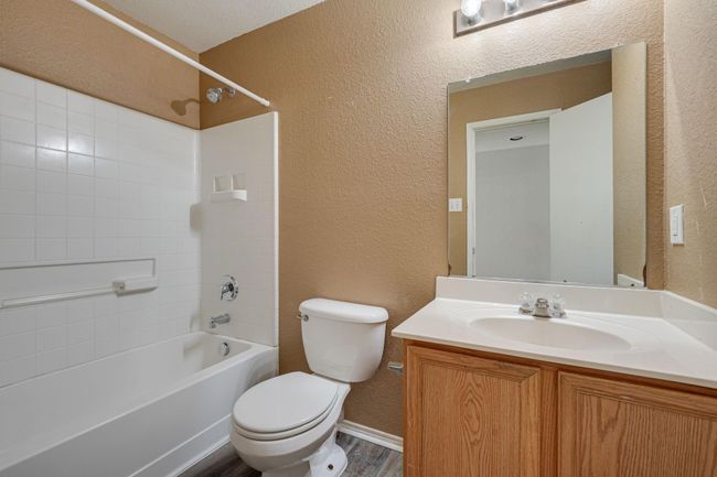 Bathroom with a textured wall, shower / washtub combination, vanity, and wood finished floors | Image 21