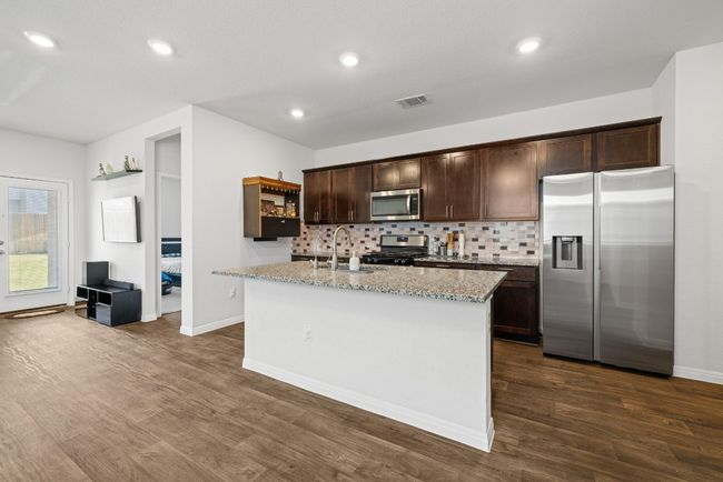 Kitchen featuring stainless steel appliances, a sink, dark brown cabinets, decorative backsplash, and dark wood-style flooring | Image 11