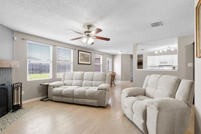 Living area featuring a ceiling fan, light wood-style flooring, a fireplace, and a textured ceiling | Image 6