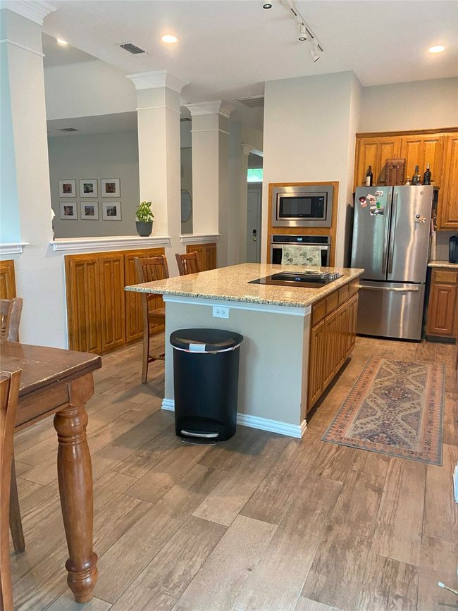 Kitchen with light stone countertops, light wood tile floors, decorative columns, a kitchen island, and appliances with stainless steel finishes | Image 13