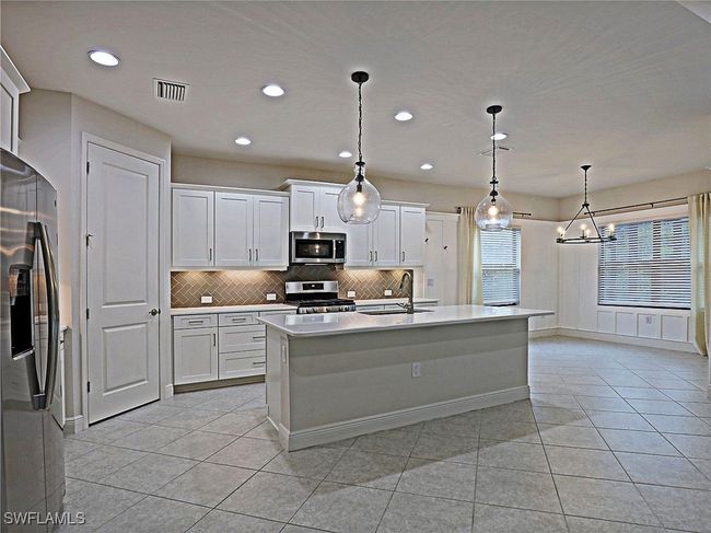 Kitchen with stainless steel appliances, a sink, decorative backsplash, light countertops, and light tile patterned floors | Image 8