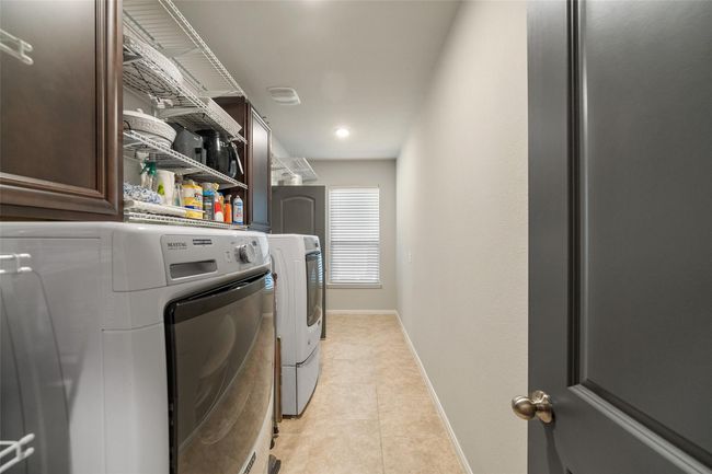 The well-organized laundry room has ample shelving for storage, and a window providing natural light. The space is compact and functional, with neutral tones and tiled flooring. | Image 30
