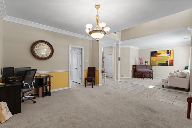 Carpeted office with ornate columns, tile patterned flooring, crown molding, baseboards, and a chandelier | Image 5