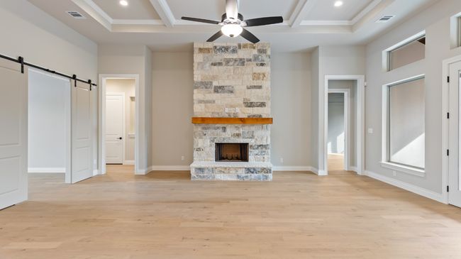 Unfurnished living room featuring a barn door, light wood-style floors, a stone fireplace, beamed ceiling, and a ceiling fan | Image 18