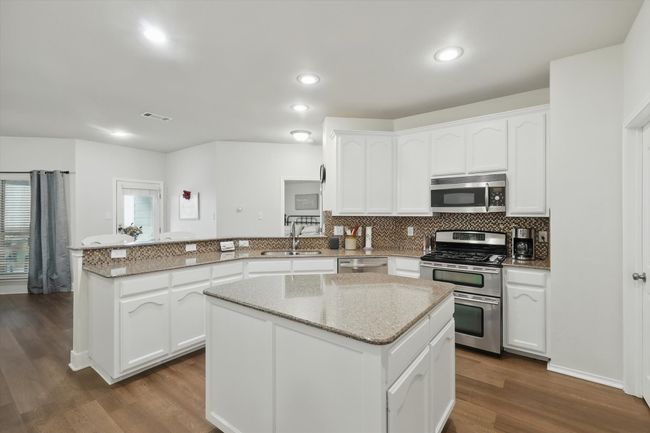Kitchen featuring stainless steel appliances, a peninsula, backsplash, white cabinetry, and light stone counters | Image 16