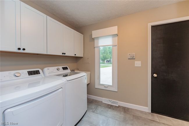 Clothes washing area with washer and dryer, cabinets, a textured ceiling, sink, and light tile flooring | Image 22