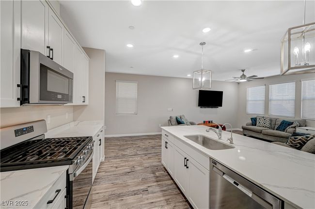 Kitchen featuring stainless steel appliances, a sink, open floor plan, light wood finished floors, and white cabinetry | Image 23