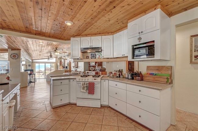 Kitchen with white gas range, wood ceiling, stainless steel microwave, under cabinet range hood, and white cabinets | Image 31