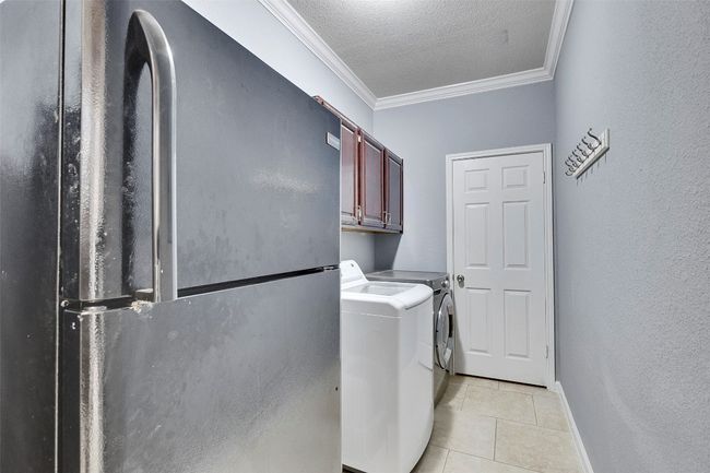 Washroom with cabinet space, washer and dryer, crown molding, light tile patterned floors, and baseboards | Image 29