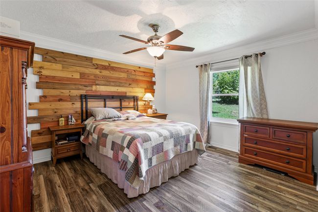 Bedroom with dark wood-type flooring, crown molding, a textured ceiling, a ceiling fan, and wood walls | Image 14