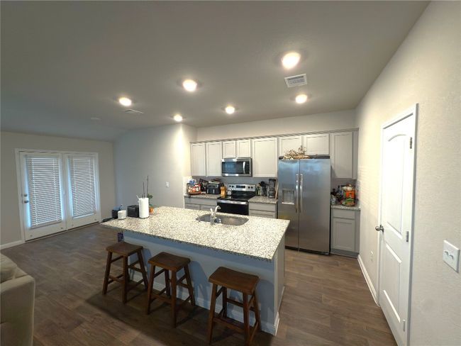 Kitchen with appliances with stainless steel finishes, dark wood finished floors, a kitchen bar, light stone counters, and a kitchen island with sink | Image 4