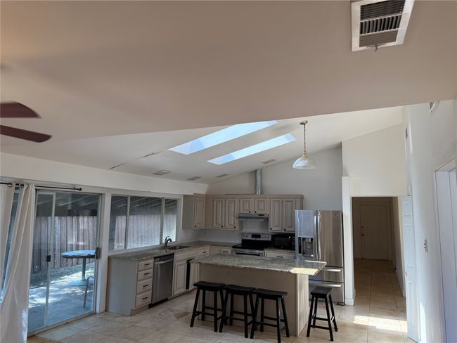 Kitchen featuring stainless steel appliances, a skylight, light tile patterned floors, a kitchen island, and a kitchen breakfast bar | Image 9