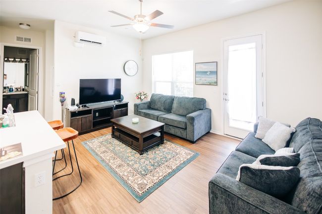 Living area with a wall mounted AC, ceiling fan, and light wood-style floors | Image 4