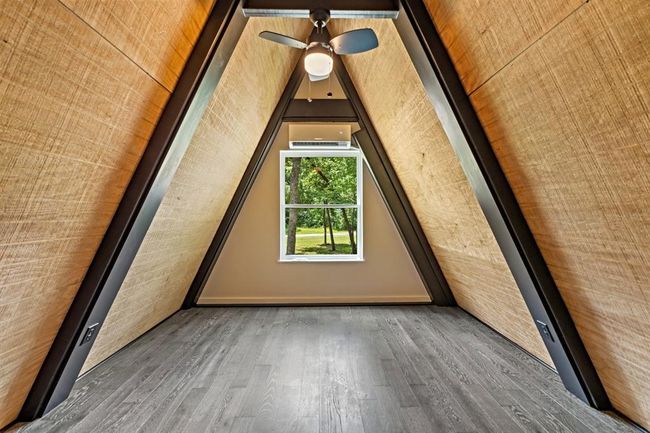 This photo shows the 2nd floor A-frame loft with warm wood paneling and sleek black beams. The space features a ceiling fan and a view of the staircase, offering a cozy, modern vibe. | Image 21