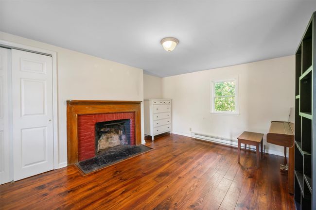 Living area with hardwood / wood-style flooring, a baseboard heating unit, a brick fireplace, and baseboards | Image 14