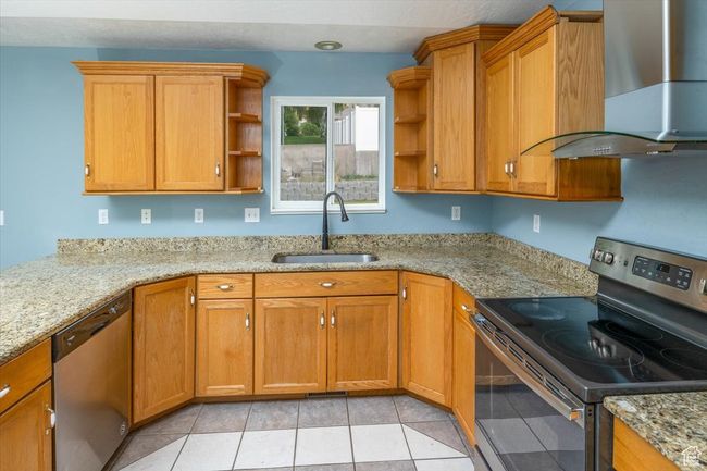 Kitchen with light tile patterned flooring, light stone counters, stainless steel appliances, sink, and wall chimney range hood | Image 14