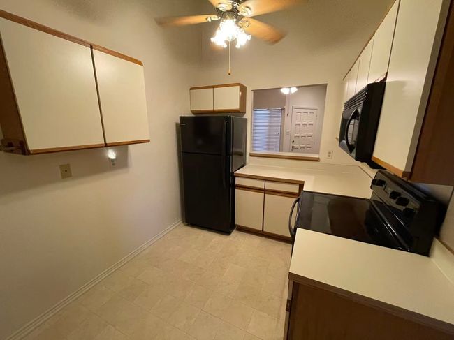 Kitchen with black appliances, a ceiling fan, light countertops, and white cabinets | Image 7