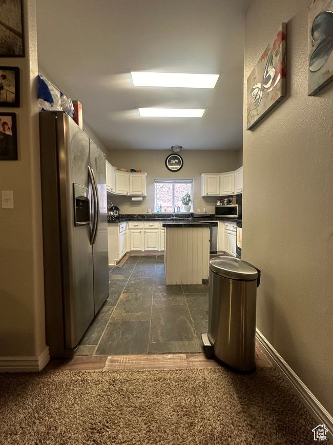Kitchen featuring stainless steel refrigerator with ice dispenser, dark stone counters, a kitchen island, dishwasher, and white cabinets | Image 7