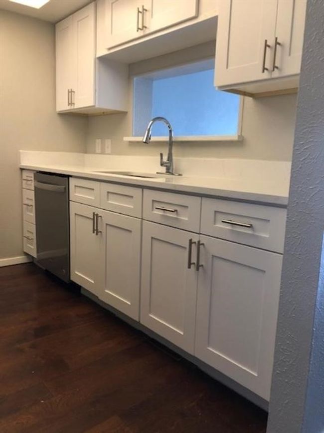 Kitchen with stainless steel dishwasher, dark wood-style floors, light countertops, and white cabinets | Image 18