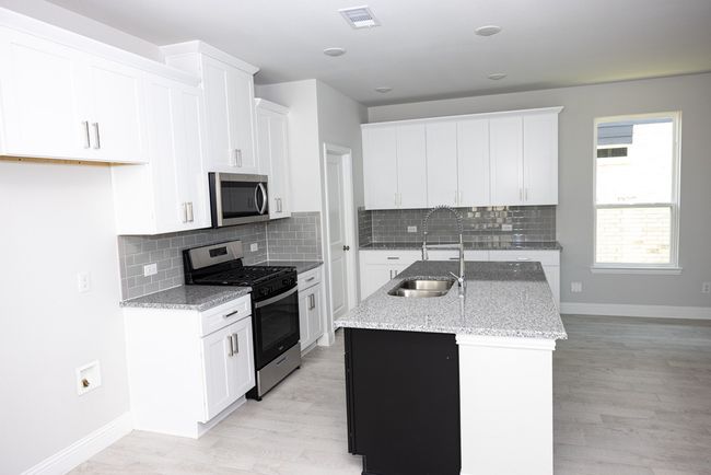 Kitchen featuring stainless steel appliances, a kitchen island with sink, backsplash, and light stone counters | Image 6