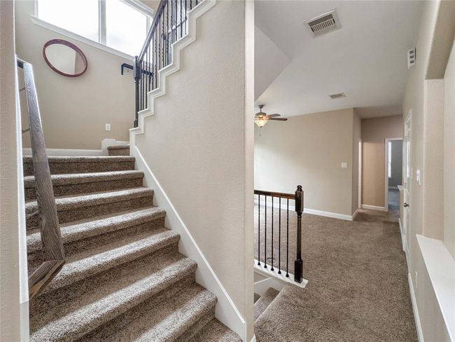 This photo showcases a bright, carpeted staircase with wooden handrails leading to a landing area. The space features neutral walls and a ceiling fan, providing a welcoming and cozy atmosphere. | Image 29