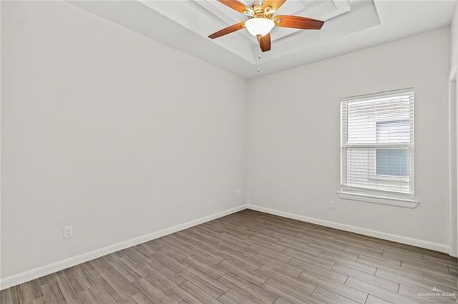 Empty room with a raised ceiling, wood finished floors, and ceiling fan | Image 6