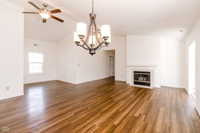 unfurnished living room featuring a fireplace with flush hearth, dark wood-style flooring, visible vents, ceiling fan with notable chandelier, and lofted ceiling | Image 6